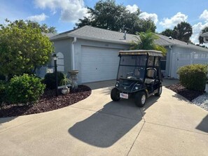 Un carrito de golf estacionado en una entrada de casa con garaje.