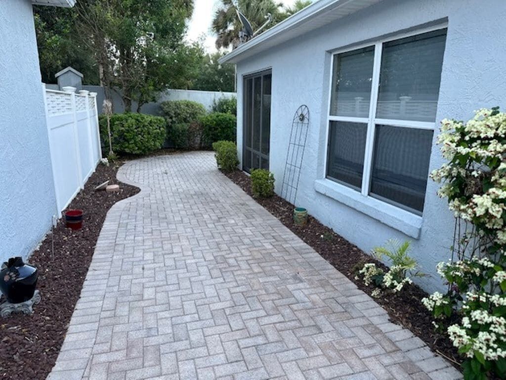 A paved pathway leading to a house with a window and a door.