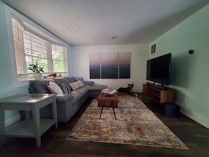 A living room with a sofa, a coffee table, a TV, and a window with blinds. - Pet friendly minutes to beach! (Middle Township)