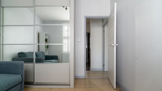 Una camera moderna con un divano grigio, un armadio a specchio e un corridoio che porta a una cabina armadio.