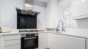 Una cucina moderna con mobili bianchi, piano cottura nero e cappa aspirante in acciaio inossidabile.