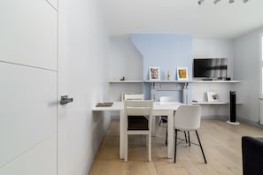 A modern kitchen with white cabinetry, a dining table, chairs, and a built-in TV.