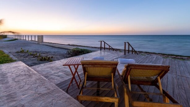 A wooden deck with two wicker chairs and a small table, overlooking a beach at sunset. - VILLA KUXTAL, OCEANFRONT (San Crisanto)