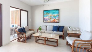 A living room with wicker furniture, a coffee table, and a painting of a beach scene. - VILLA KUXTAL, OCEANFRONT (San Crisanto)