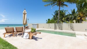 A poolside area with lounge chairs, a palm tree, and a view of the ocean. - VILLA KUXTAL, OCEANFRONT (San Crisanto)