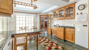 A modern kitchen with wooden cabinets, a glass dining table, and a colorful rug.