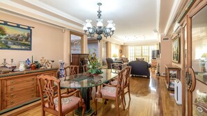 A spacious dining area with a glass table, wooden chairs, and a chandelier.