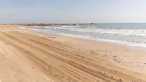 A sandy beach with gentle waves, a rocky breakwater, and a clear sky.