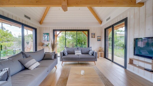 Ein geräumiges Wohnzimmer mit zwei grauen Sofas, einem Holztisch und einem an der Wand montierten Fernseher.