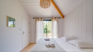 Ein Schlafzimmer mit Bett, einem fenster mit Vorhängen, einer Holzbalkendecke und einer Wandleuchte.