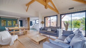 Ein geräumiger Wohnbereich mit Holzboden, einem grauen Sofa, einem Esstisch und einer Küche im Hintergrund.