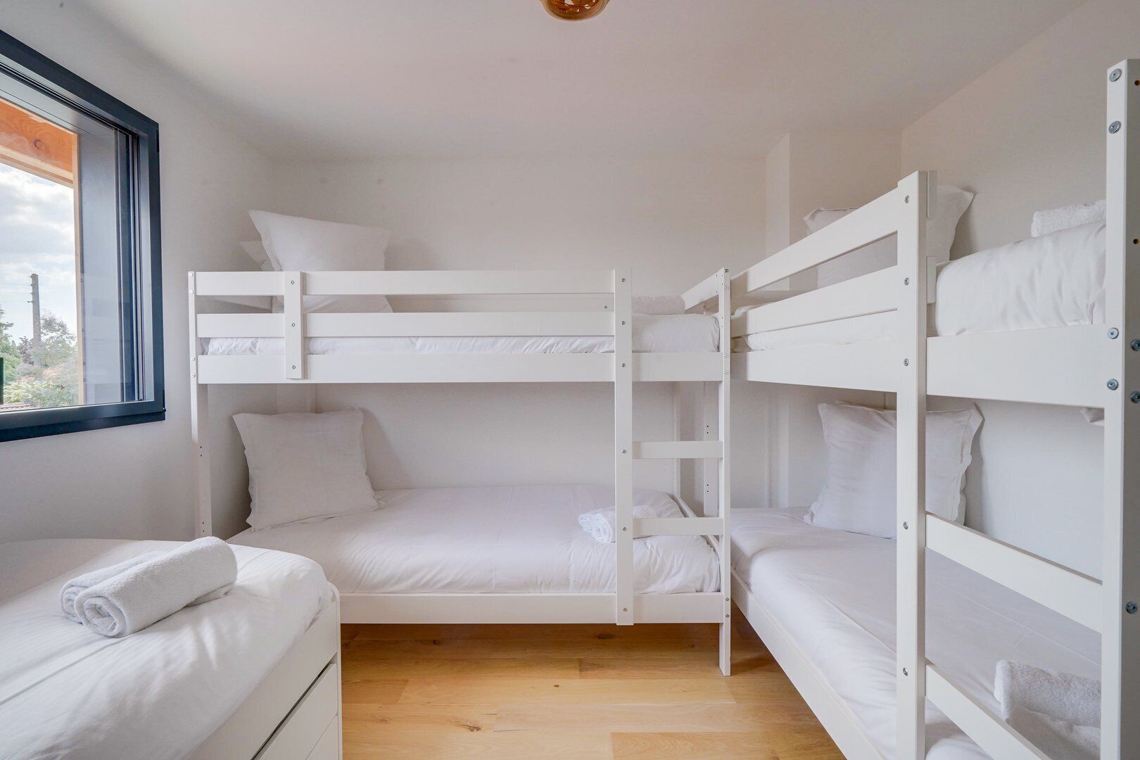 A bunk bed room with white bedding and a window with a view of greenery.