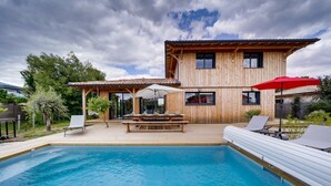 Ein Holzhaus mit Swimmingpool, Außenmöbeln und einer Pergola.