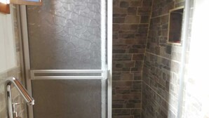 A bathroom with a stone wall, a glass shower enclosure, and a white sink. - Cabañas Alpina  (San Agustin)