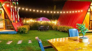 An outdoor seating area with a table and chairs, surrounded by a red structure and string lights. - Cabañas Alpina  (San Agustin)