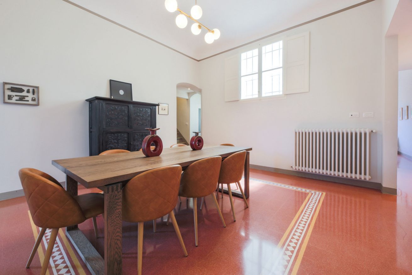 A dining area with a wooden table, four chairs, a radiator, and a patterned rug.