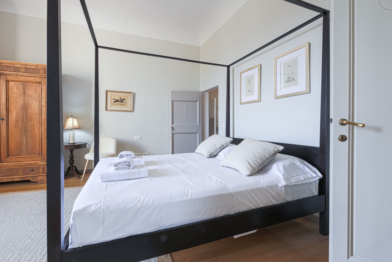 A four-poster bed with white linens, a wooden wardrobe, and framed artwork on the walls.