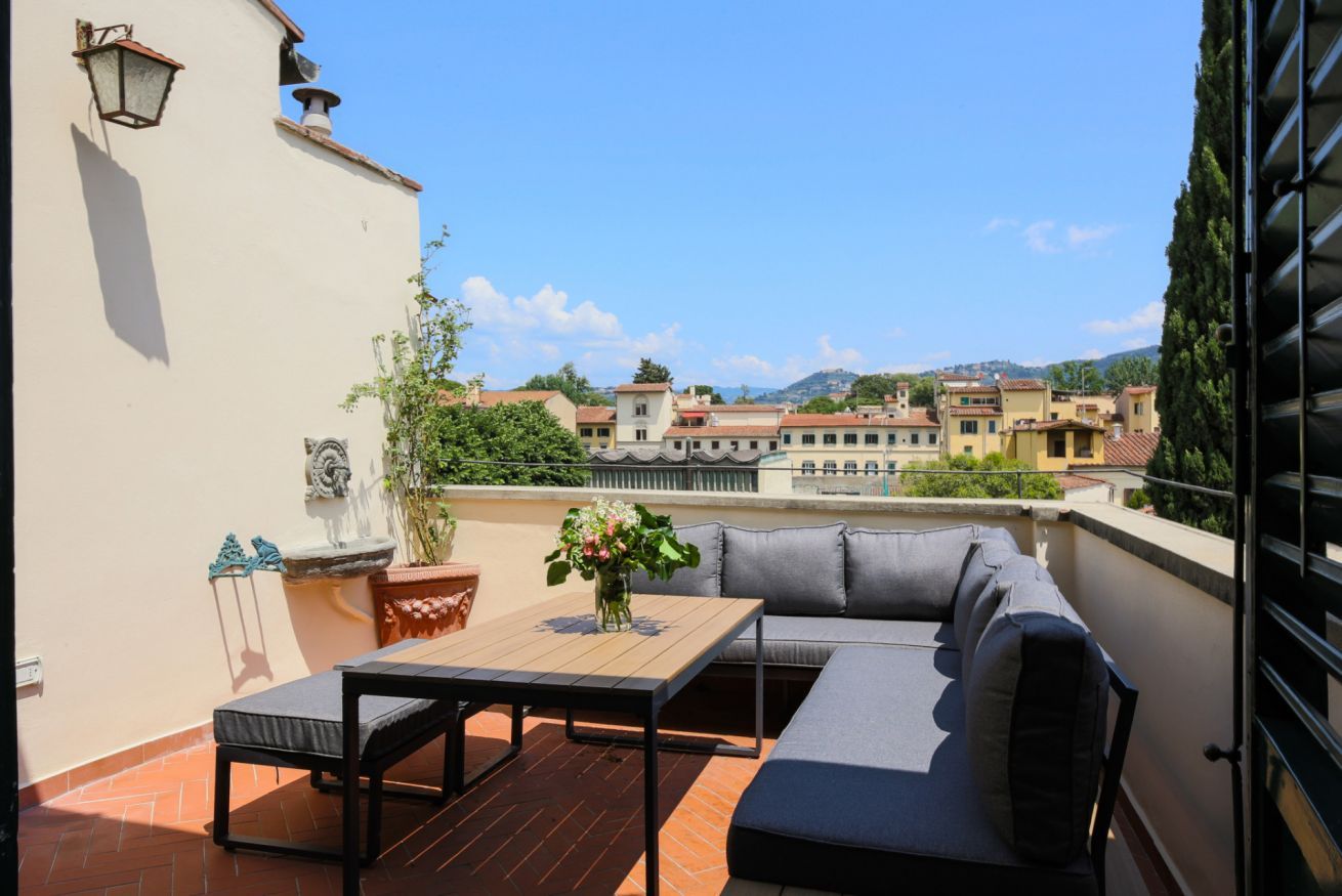 A rooftop terrace with a sofa, table, and potted plants.