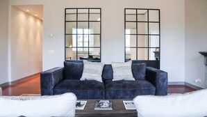 Een woonkamer met een donkerblauwe bank, witte kussens, een salontafel met tijdschriften en een groot raam met uitzicht.