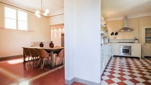 Een keuken met witte kastjes, een rood-wit geruit vloertje, en een eethoek met stoelen en een tafel.