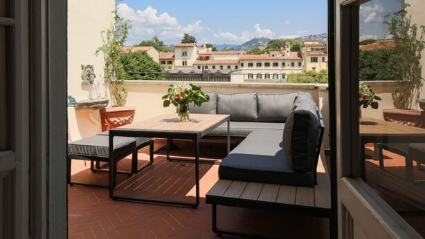 Een balkon met een bank, een tafel en plantenpotten.