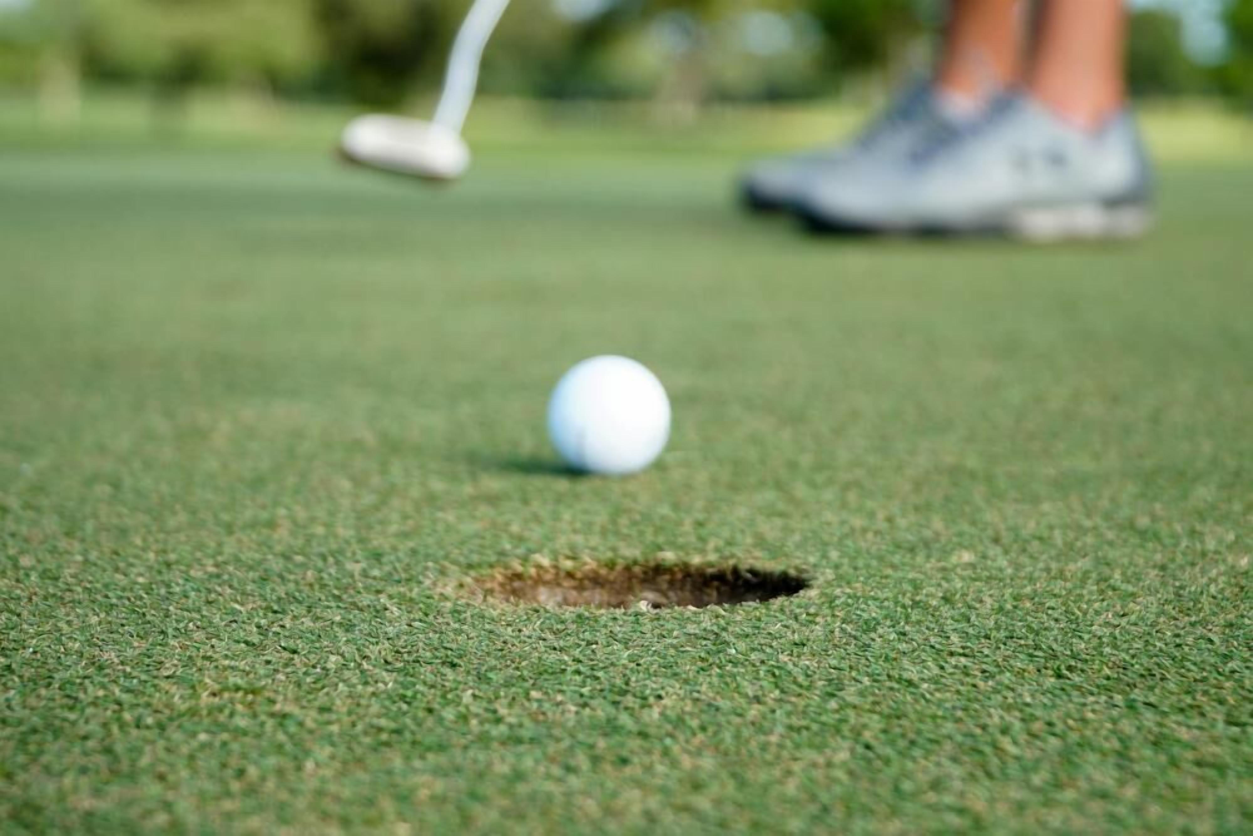 Ein Golfball auf einem Grün, in der Nähe ein Loch.
