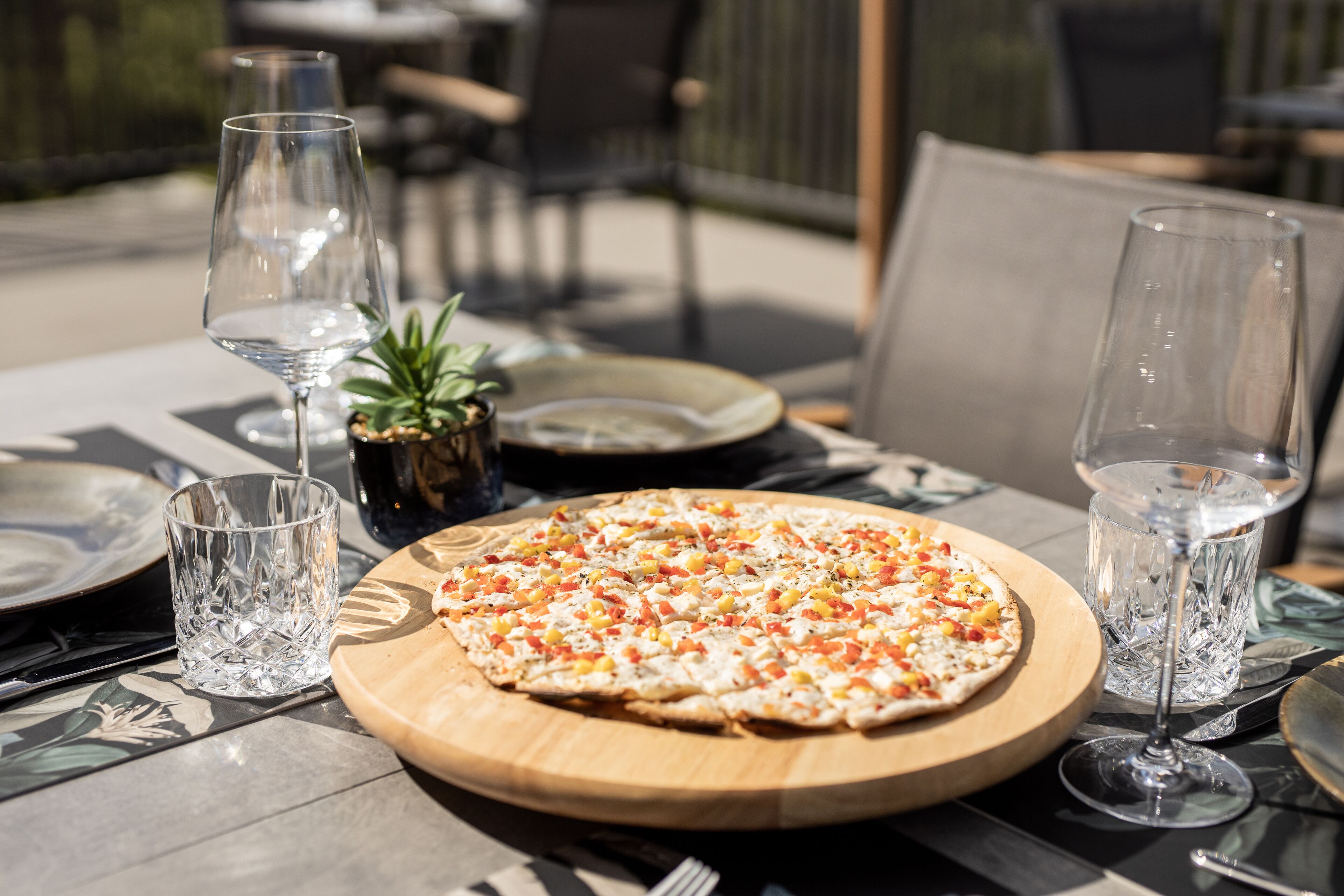 En pizza på en träbricka, tillsammans med ett glas vatten och ett glas vin på ett bord.