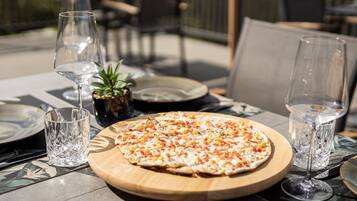 En pizza på en träbricka, tillsammans med ett glas vatten och ett glas vin på ett bord.