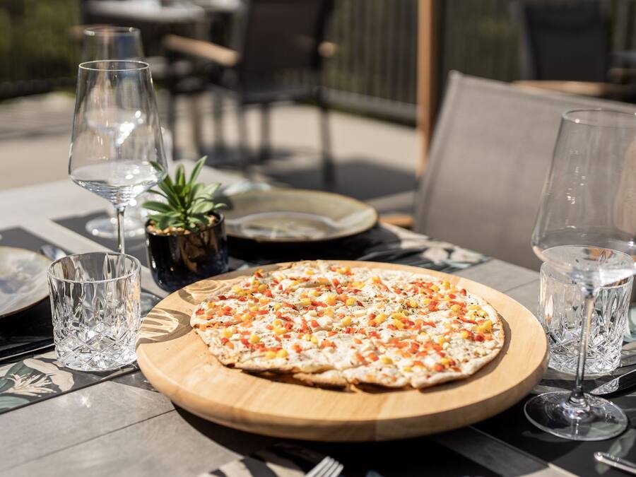 A pizza on a wooden board with a glass of water and a glass of wine on a table.