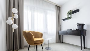 Una habitación moderna con un sillón dorado, una mesita redonda pequeña, una lámpara de pie, una estación de café y cortinas traslúcidas.