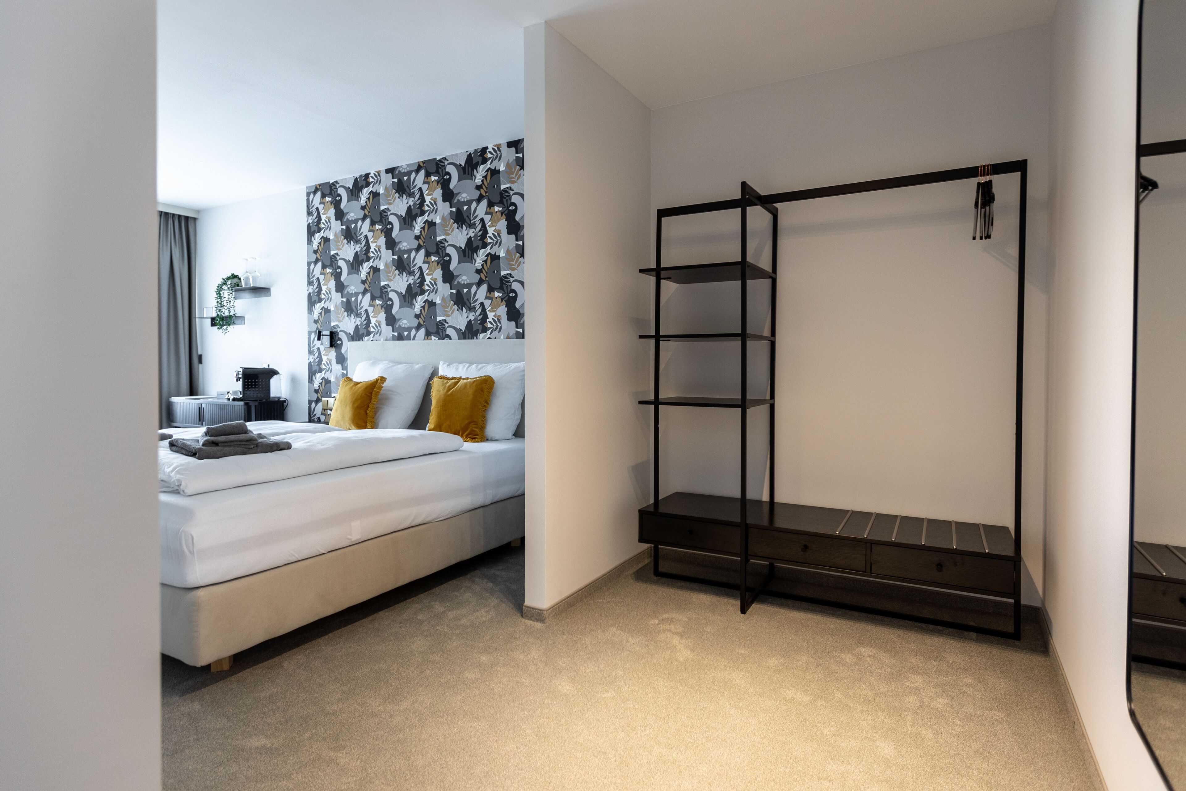A modern bedroom with a bed, a black metal shelf unit, and a patterned wall.