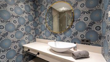 Un baño con un lavamanos blanco, un espejo redondo y papel tapiz estampado.