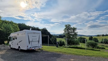Ein weißer Wohnmobil auf einem Schotterweg mit schöner Aussicht auf grüne Felder und Bäume im Hintergrund.