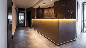 Un área de recepción moderna con un mostrador oscuro, una pared de acento de piedra y una puerta de cristal que da a un balcón.