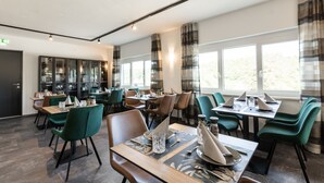 Un área de comedor moderna con sillas verdes, mesas de madera y un ventanal con cortinas.