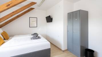 Un dormitorio con una cama, un armario gris, un cubo de basura negro y una cita motivacional enmarcada en la pared.