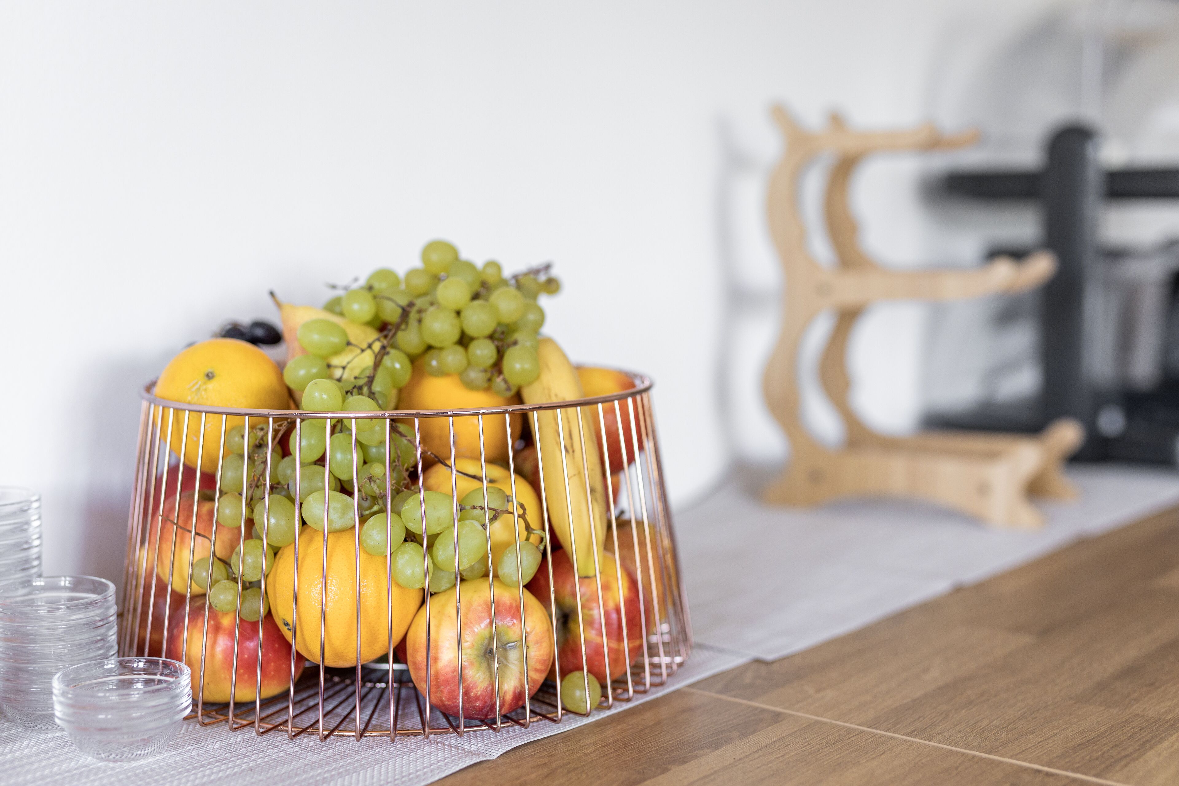 A fruit basket with apples, oranges, and grapes on a wooden table.