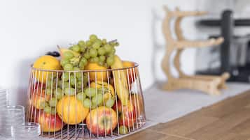 A fruit basket with apples, oranges, and grapes on a wooden table.