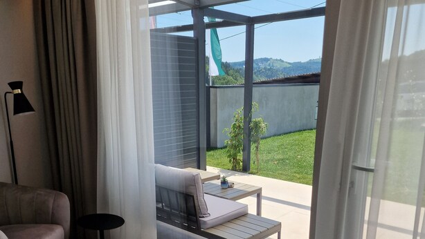 Una sala de estar moderna con un sofá, una mesita redonda y vistas a un paisaje verde a través de un ventanal corredera.