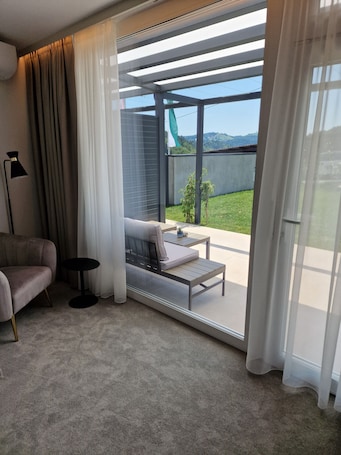 A modern living room with a sofa, a small round table, and a view of a green landscape through a sliding glass door.