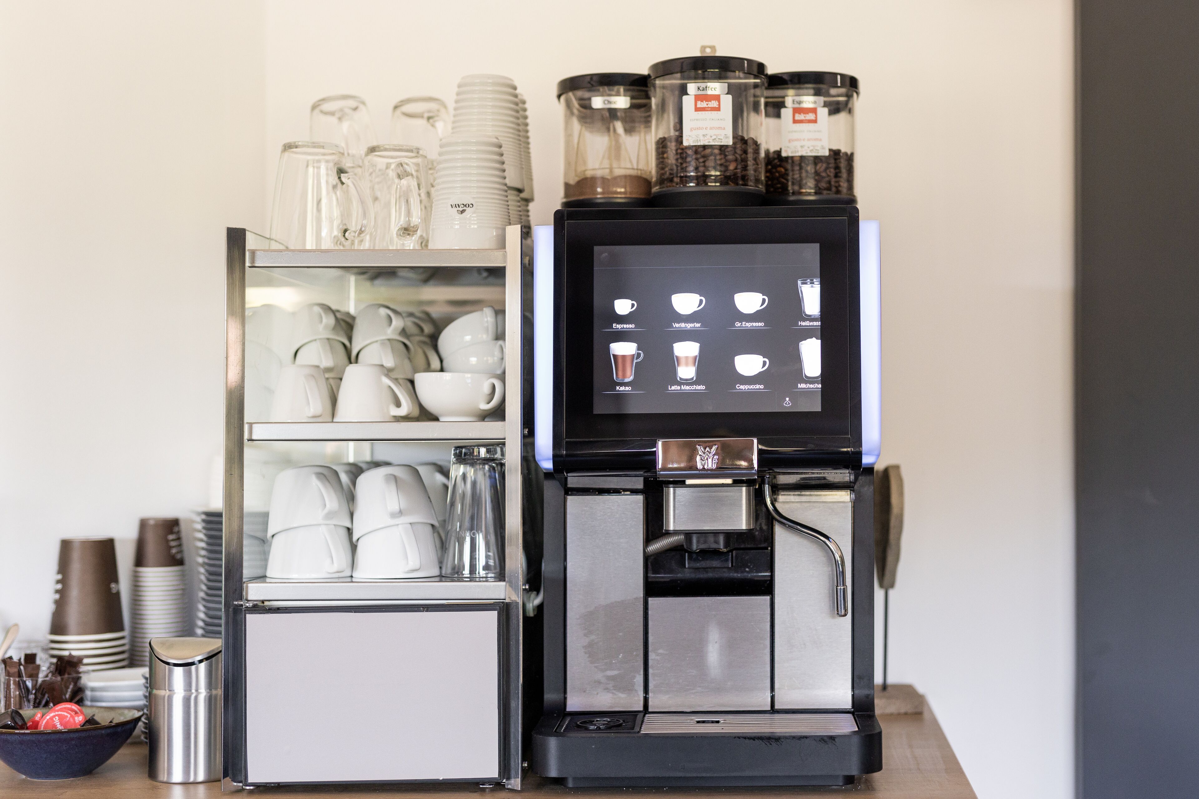 A coffee machine with a digital display menu, a coffee grinder, and a coffee press.