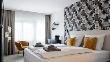 A hotel room with a large bed, two pillows, a bedside table, a chair, a desk, and a wall with a patterned design.