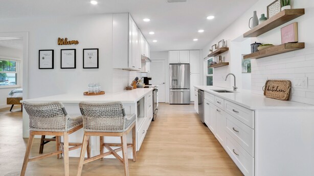 Een moderne keuken met witte kasten, een roestvrijstalen koelkast en een ontbijtbalk met rieten stoelen.