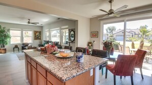 A spacious kitchen with a granite countertop, wooden cabinets, and a dining area with red chairs. - 2 Mi to Coachella: Indio Home w/ Outdoor Oasis (Indio)