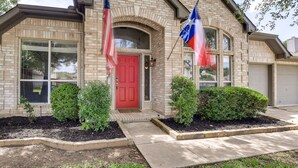 Une maison en briques avec une porte rouge, deux drapeaux et un jardin bien entretenu.