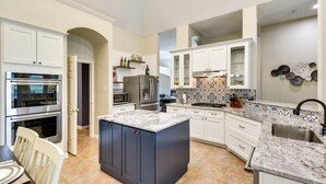 Une cuisine moderne avec des meubles blancs, un îlot central et un four encastré.