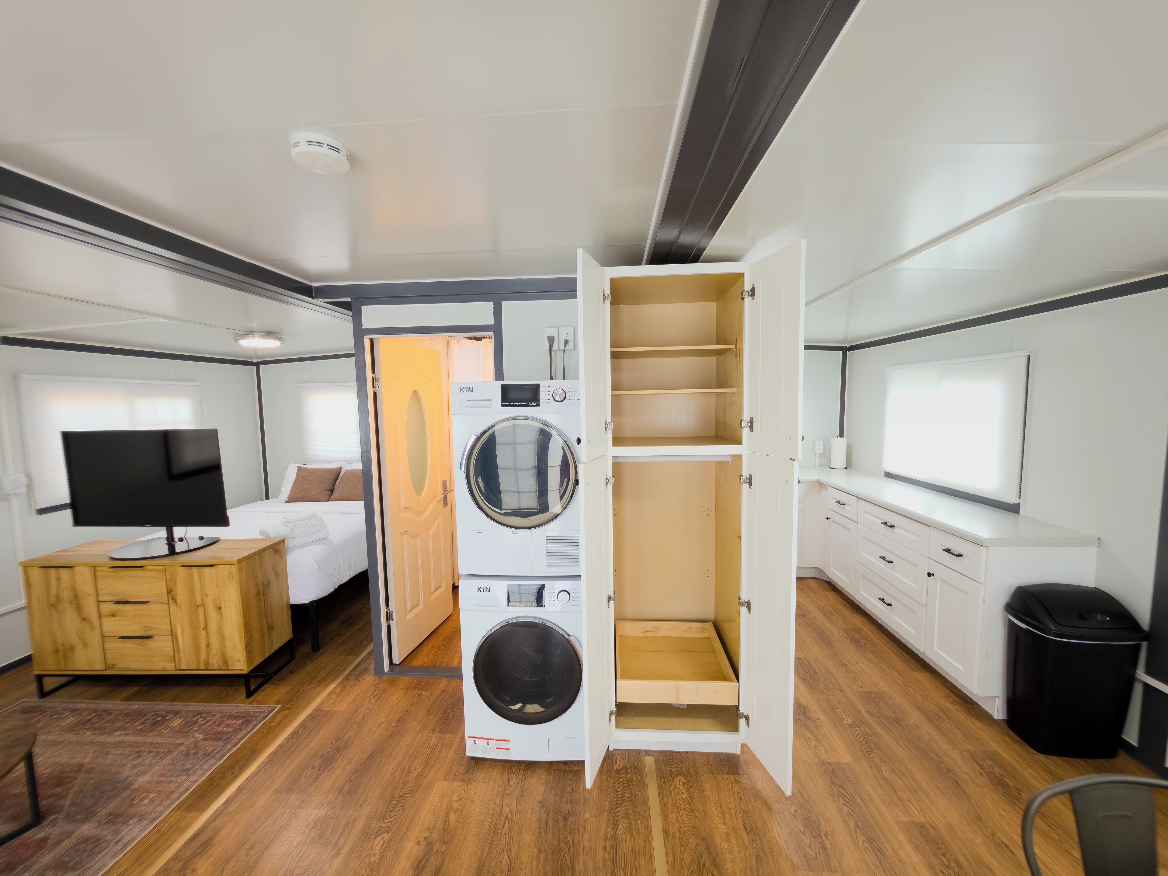 Une chambre d’hôtel compacte comprenant un lit, une télévision, un lave-linge et une petite kitchenette.