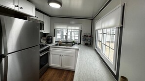 Une cuisine compacte avec des meubles blancs, un réfrigérateur en acier inoxydable, une cuisinière à gaz et une fenêtre qui laisse entrer la lumière naturelle.