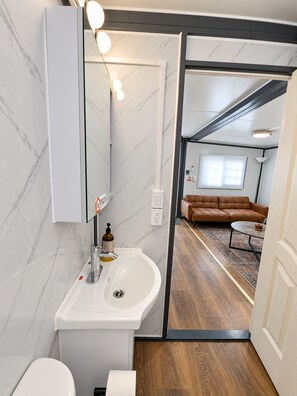 A modern bathroom with a white sink, mirror, and marble walls. - BoxHouse Executive Queen Suite (Monahans)