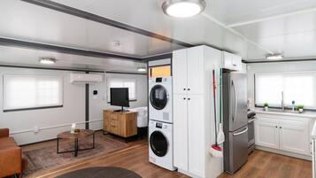 Interior modern d'un autocaravana amb cuina, rentadora, nevera i televisió de pantalla plana.